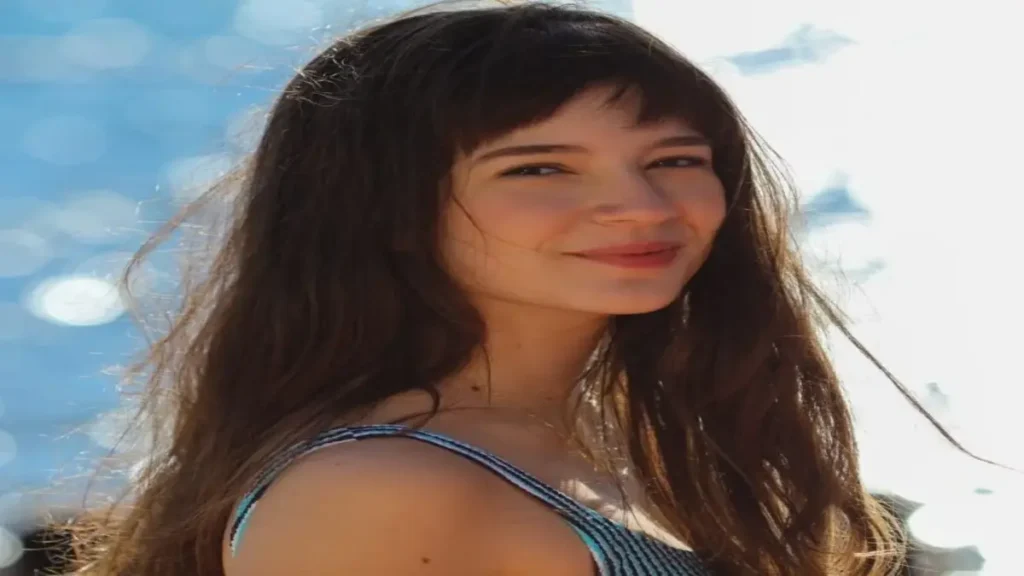 Young woman with long dark hair smiling softly outdoors in natural sunlight