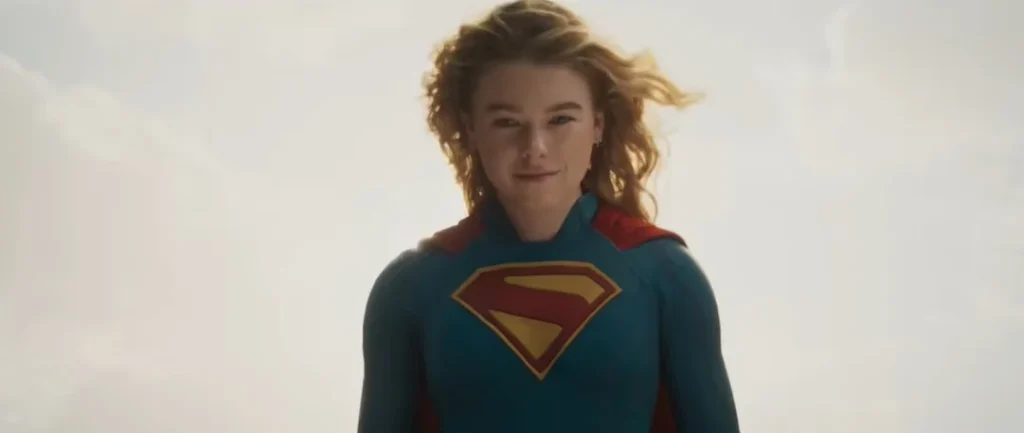 Female superhero in blue suit with iconic emblem standing confidently against the sky