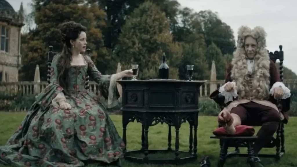 Savage House trailer scene showing two aristocratic figures seated outdoors in a tense garden setting