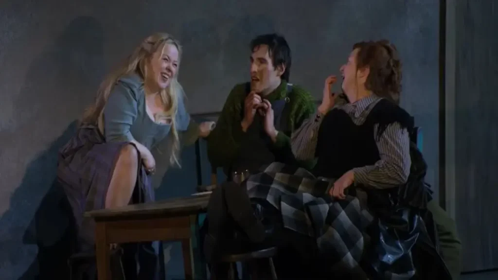 Stage scene from The Playboy of the Western World National Theatre Live showing three actors in a lively Irish pub setting