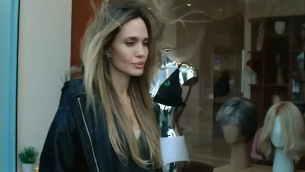 Angelina Jolie in the Couture (2026) official trailer standing inside a luxury fashion studio with flowing hair and couture wigs in the background.
