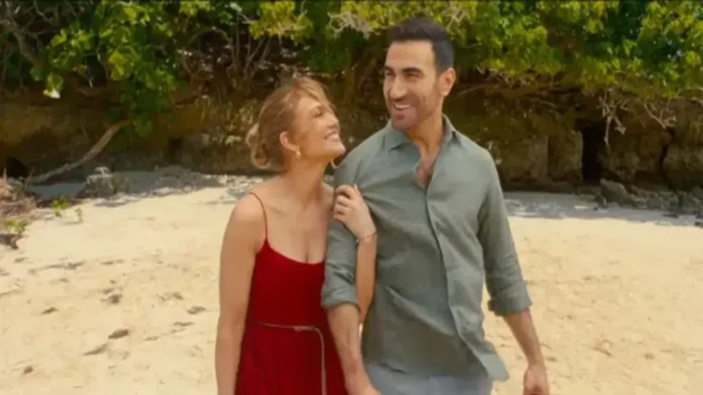 Jennifer Lopez and Brett Goldstein walking together on a beach in Office Romance Netflix trailer