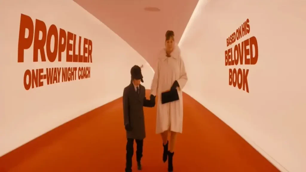 Woman and child walking through a surreal red-and-white hallway in Propeller One-Way Night Coach official trailer on Apple TV.