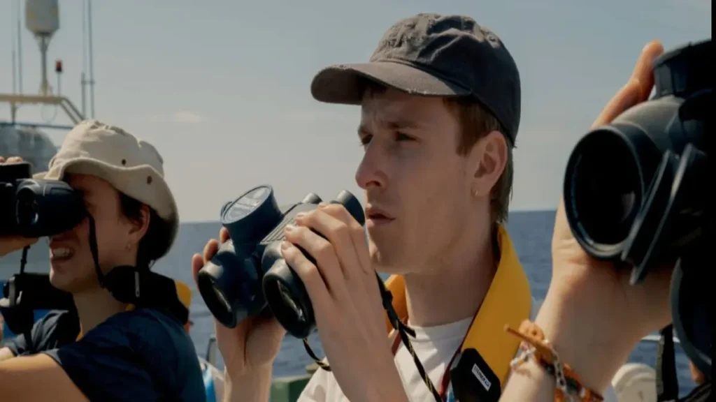 Young marine researchers using binoculars during an ocean conservation expedition featured in Netflix's 23,000 Lives documentary.